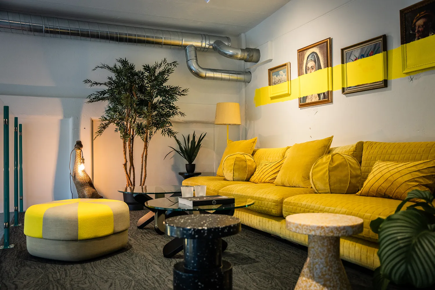 Verkshöjden, loungedel med gula soffa och tavlor på väggen övermålade med ett tjockt gult streck.